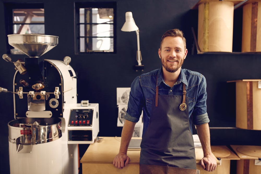 A coffee roaster smiling in front of coffee roasting machinery